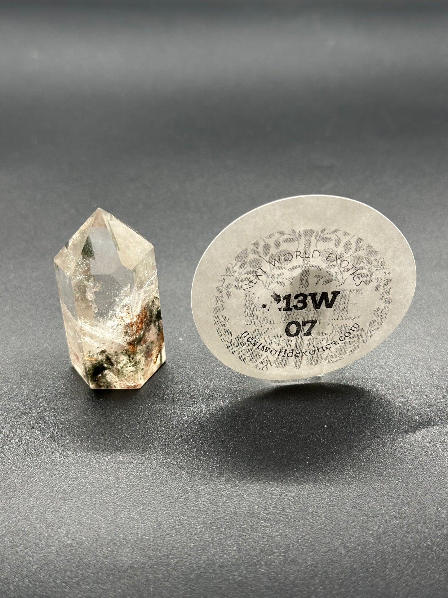 Garden Quartz Tower (213W07) features a clear crystal with brown specks, accompanied by a round white disc, showcasing its unique mineral structure.