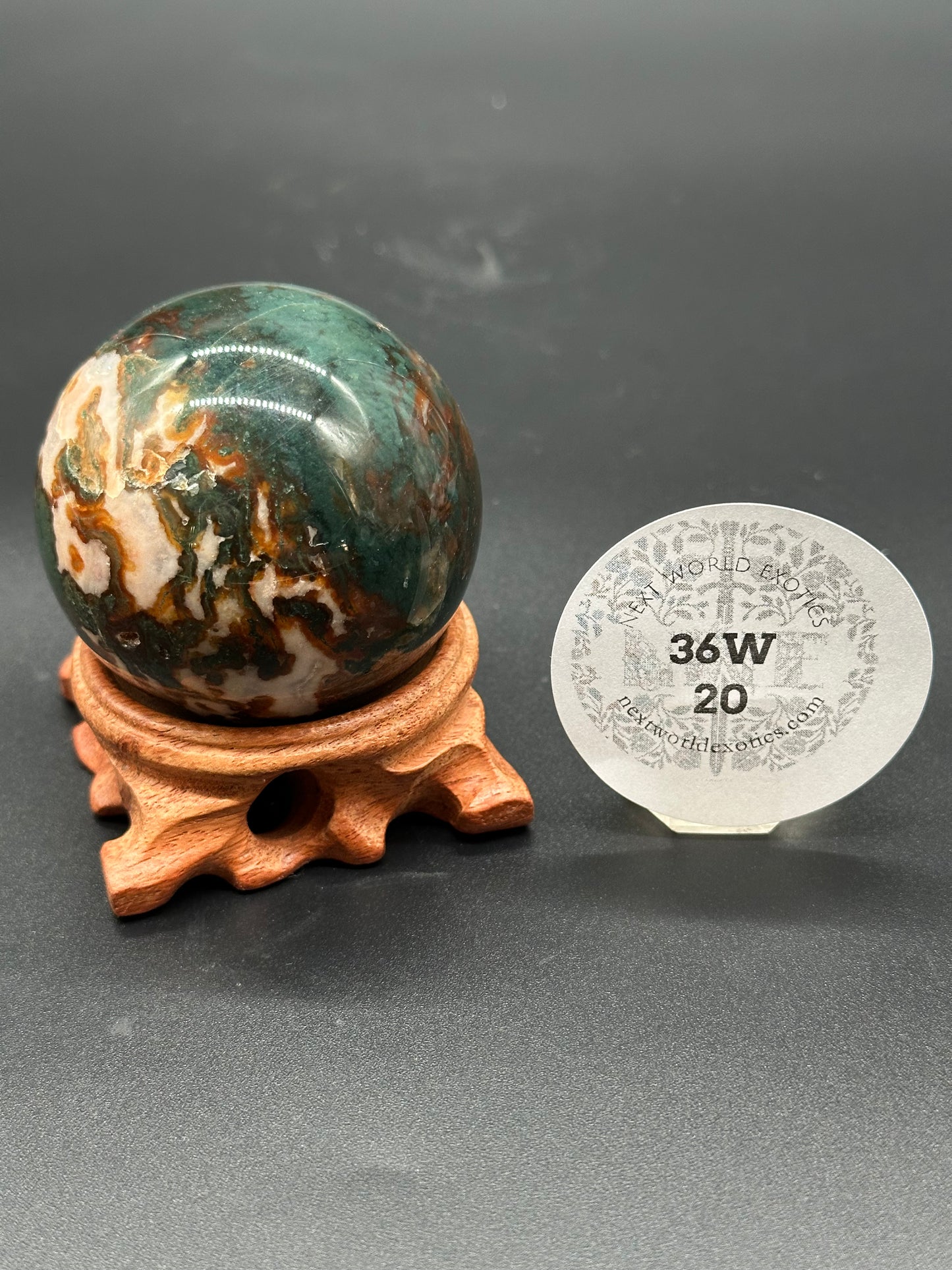 Red Moss Agate Sphere (36W20) displayed on a wooden stand beside a white circular object with black text and numbers.
