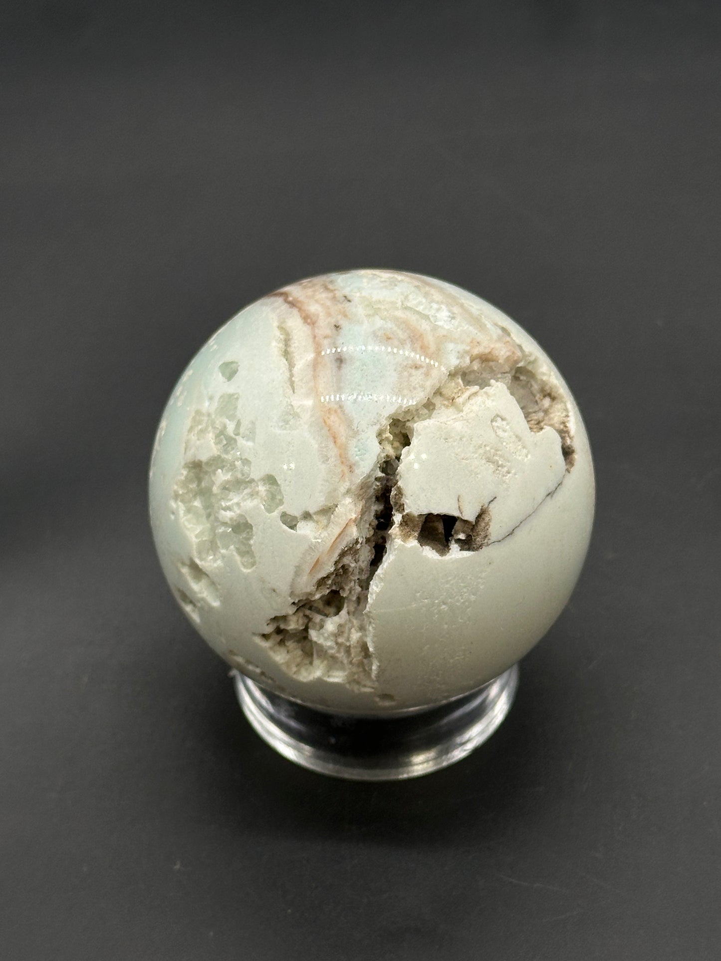 Caribbean Calcite Sphere (812W02) featuring a polished exterior with a rough, druzy-like interior, displayed on a clear stand.