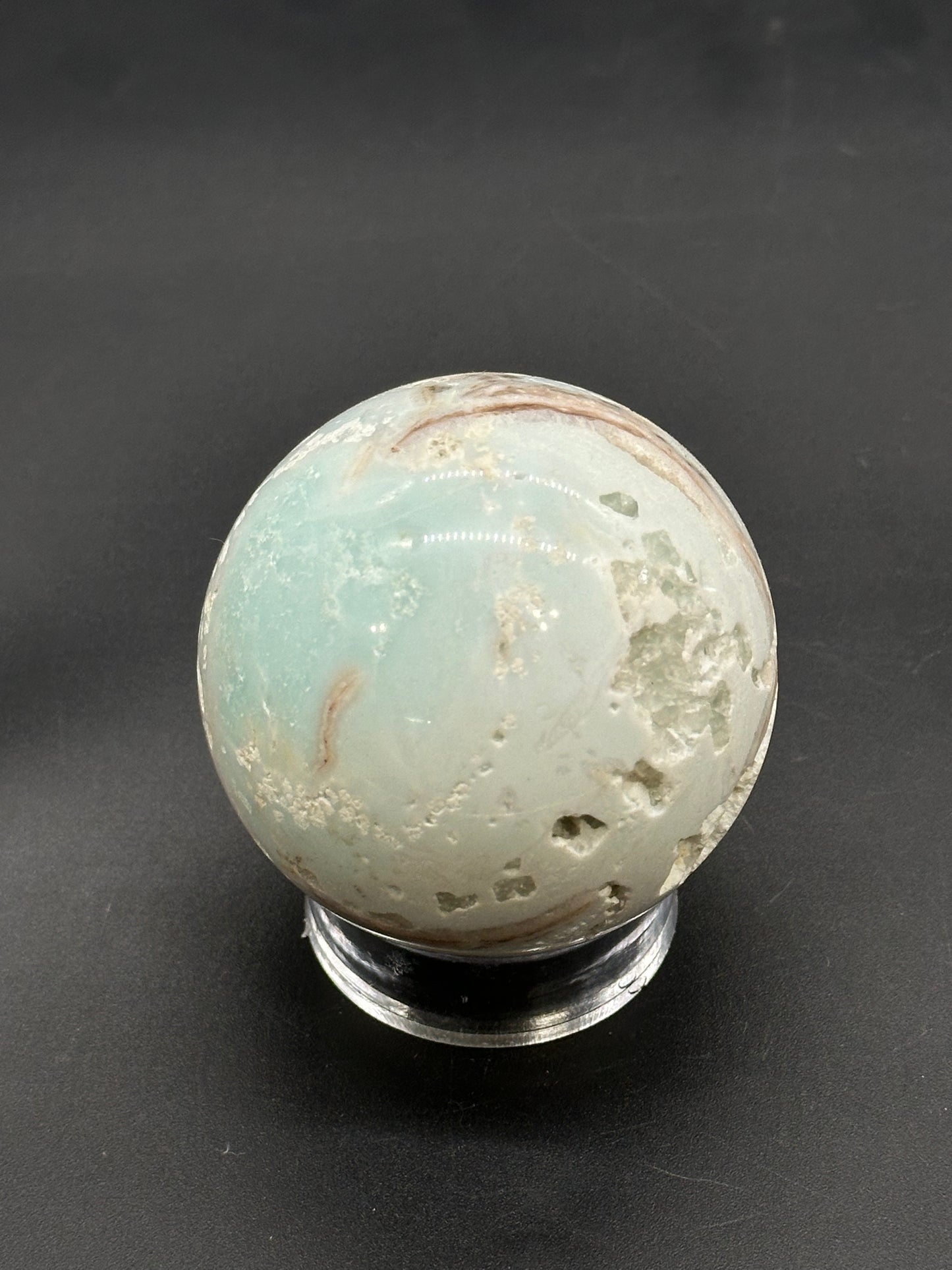 Caribbean Calcite Sphere (812W02) features a polished aqua-green surface with natural brown veins and small cavities, resting on a clear display stand.