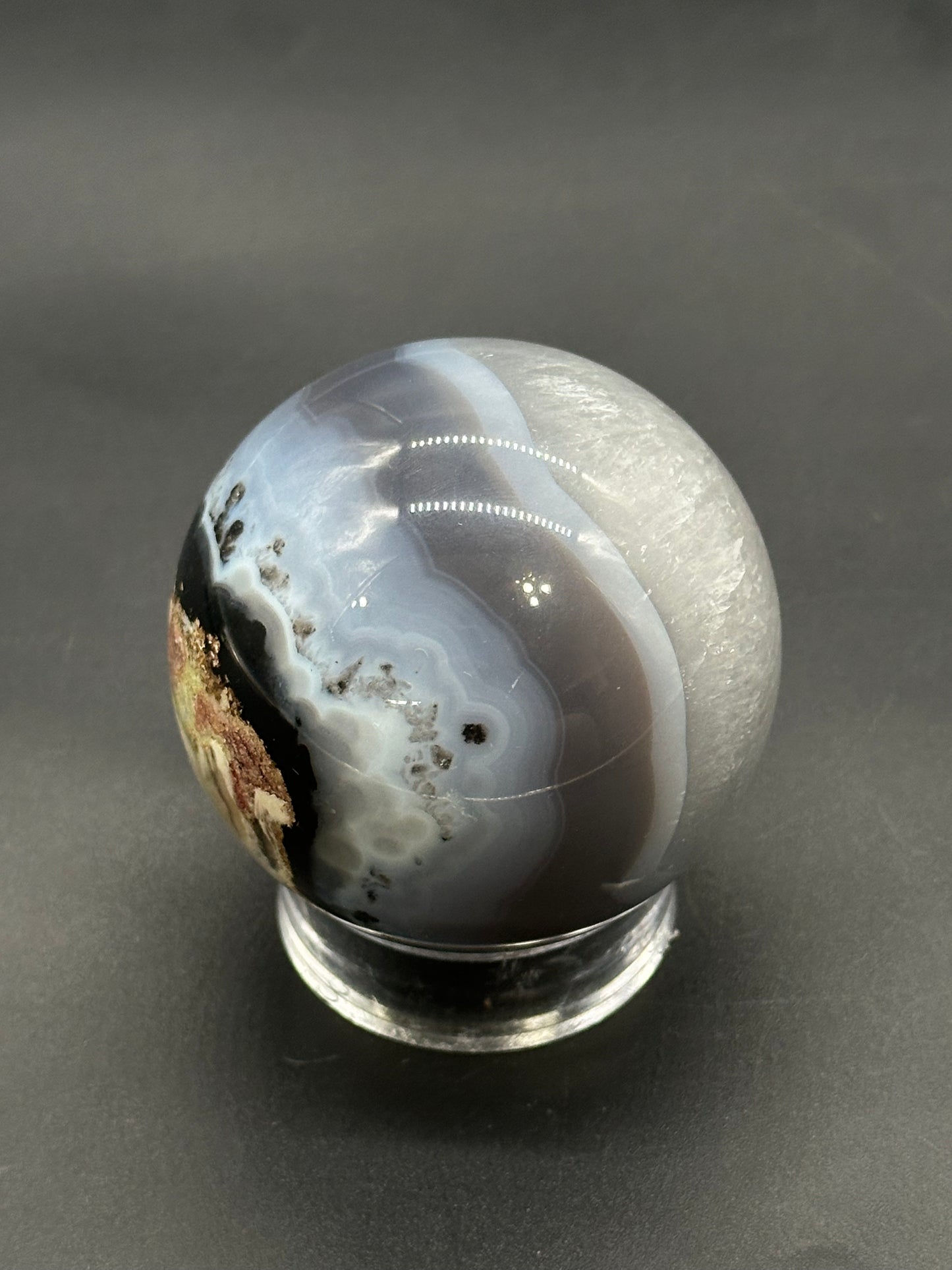 Volcanic Agate Sphere (812W03) on a clear stand, showcasing gray and white concentric layers with a crystalline pocket, embodying its unique mineral allure.