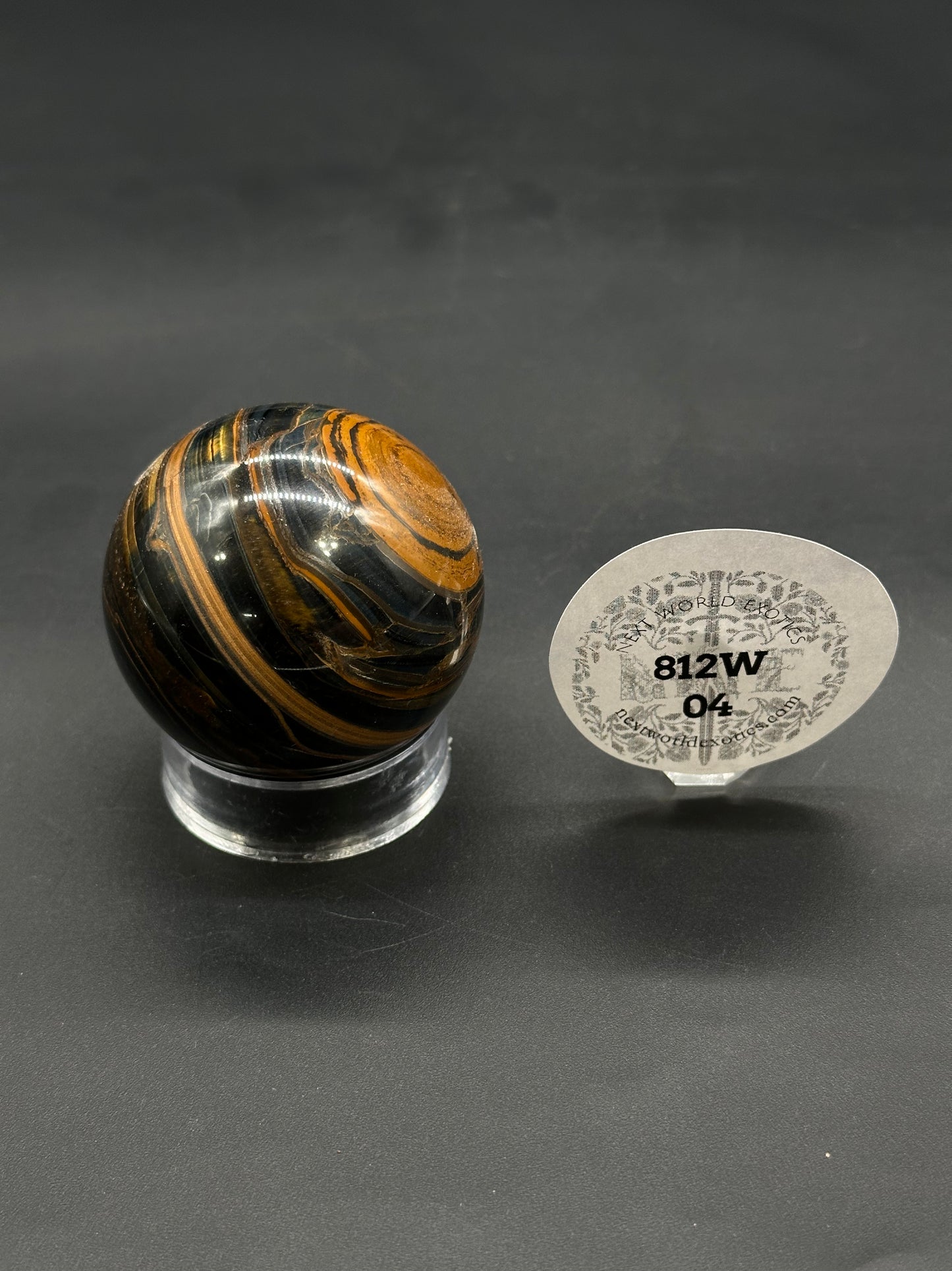 Tigers Iron Sphere (812W04) with black and golden-brown stripes on a clear acrylic stand. Oval tag reads “812W 04” from newworldexotics.com.