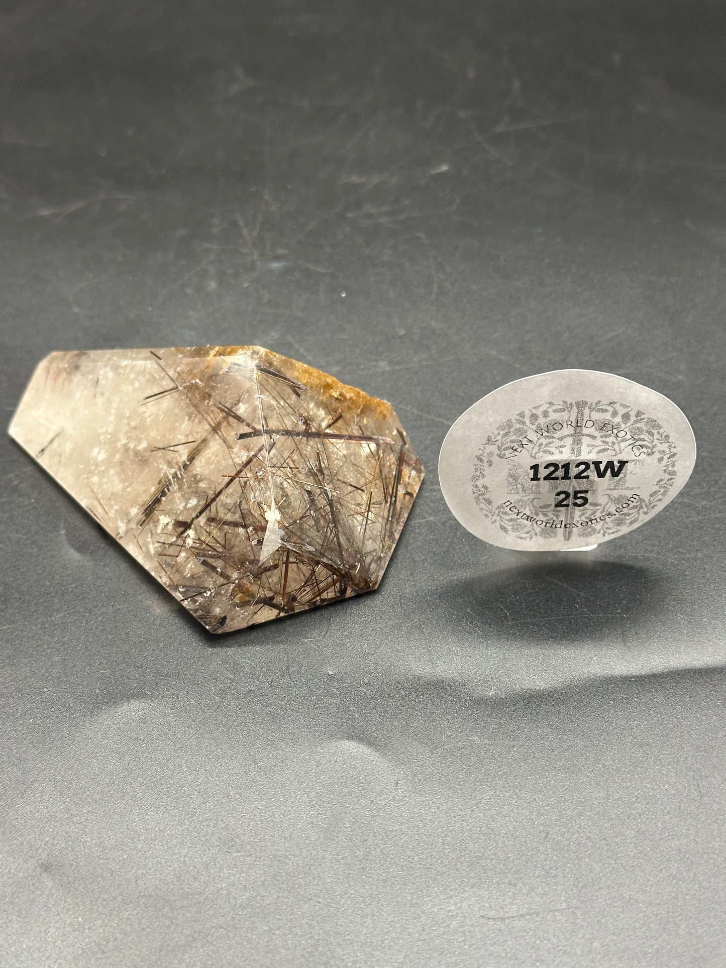 Black Rutilated Quartz (1212W25) alongside a round object, emphasizing the crystal's intricate patterns and textures.