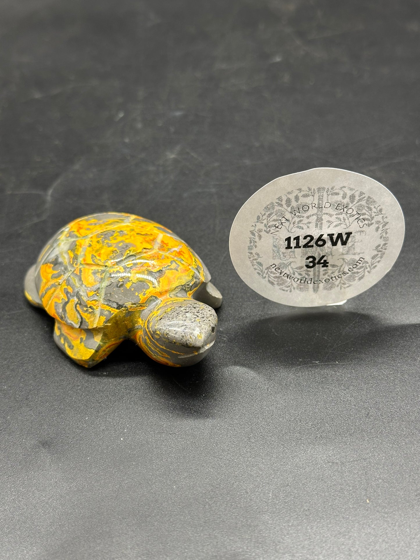 Bumblebee Jasper Turtle Carving (1126W34) displayed with a round paper tag and sticker, featuring intricate stone details in a small figurine form.