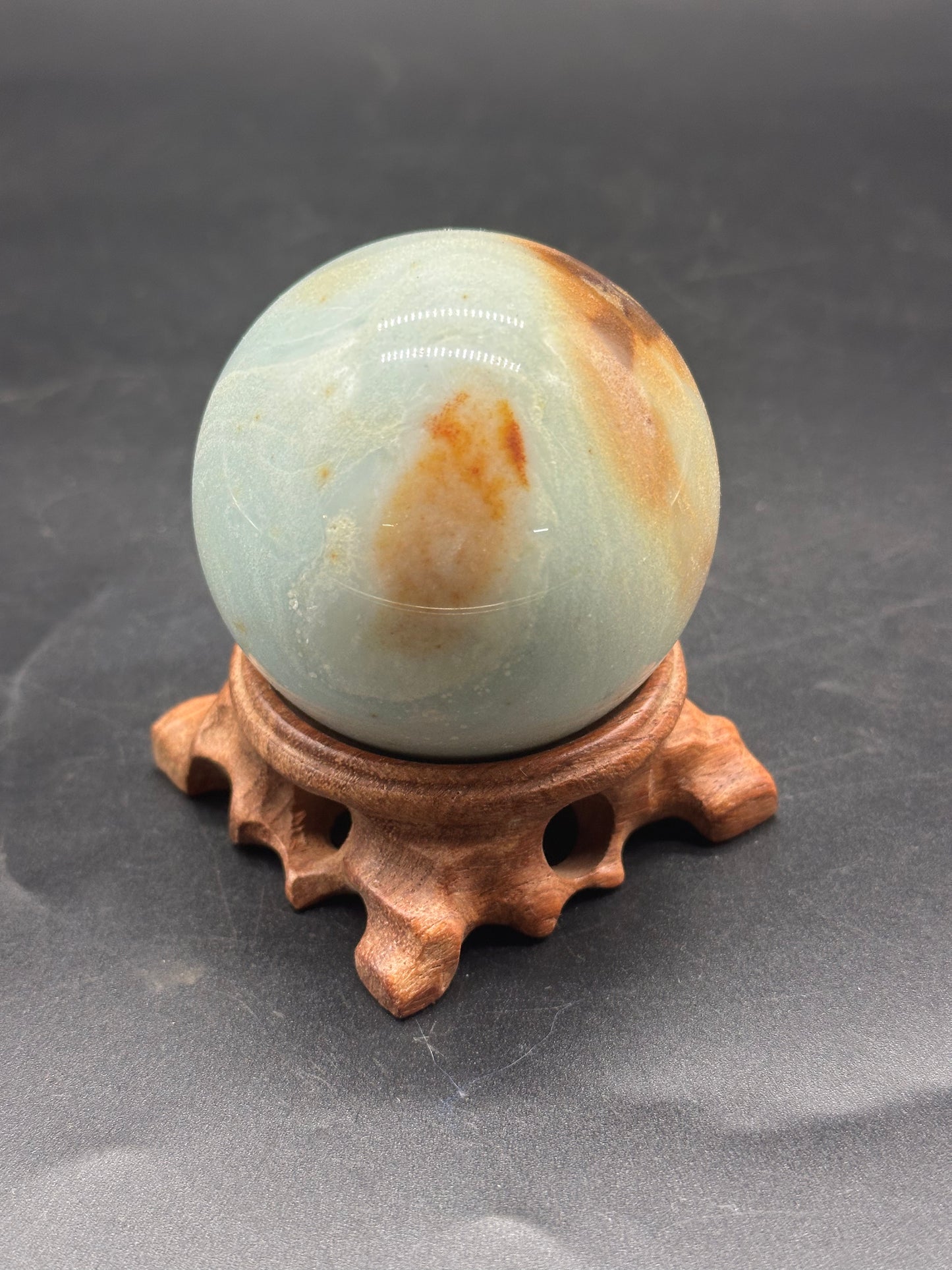 Carribbean Calcite Sphere (1212W21) displayed on a wooden stand, showcasing its smooth, rounded surface, ideal for decorative or mineral collection purposes.