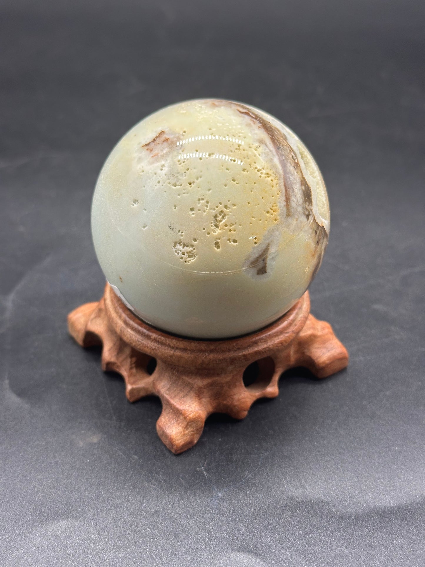 Carribbean Calcite Sphere (1212W21) on a wooden stand, showcasing its smooth, round form and natural texture.