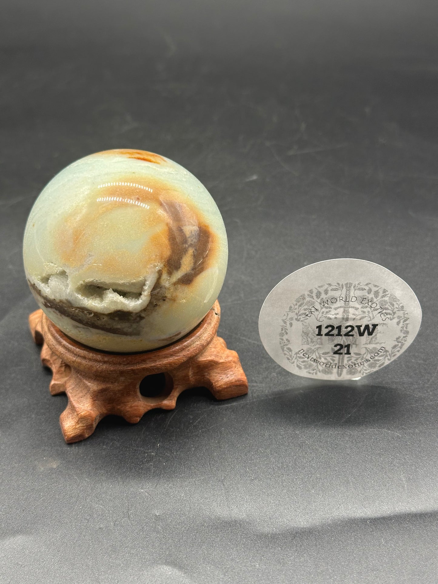 Carribbean Calcite Sphere (1212W21) displayed on a stand, alongside another round stone. A sticker with numbers is also visible in the background.