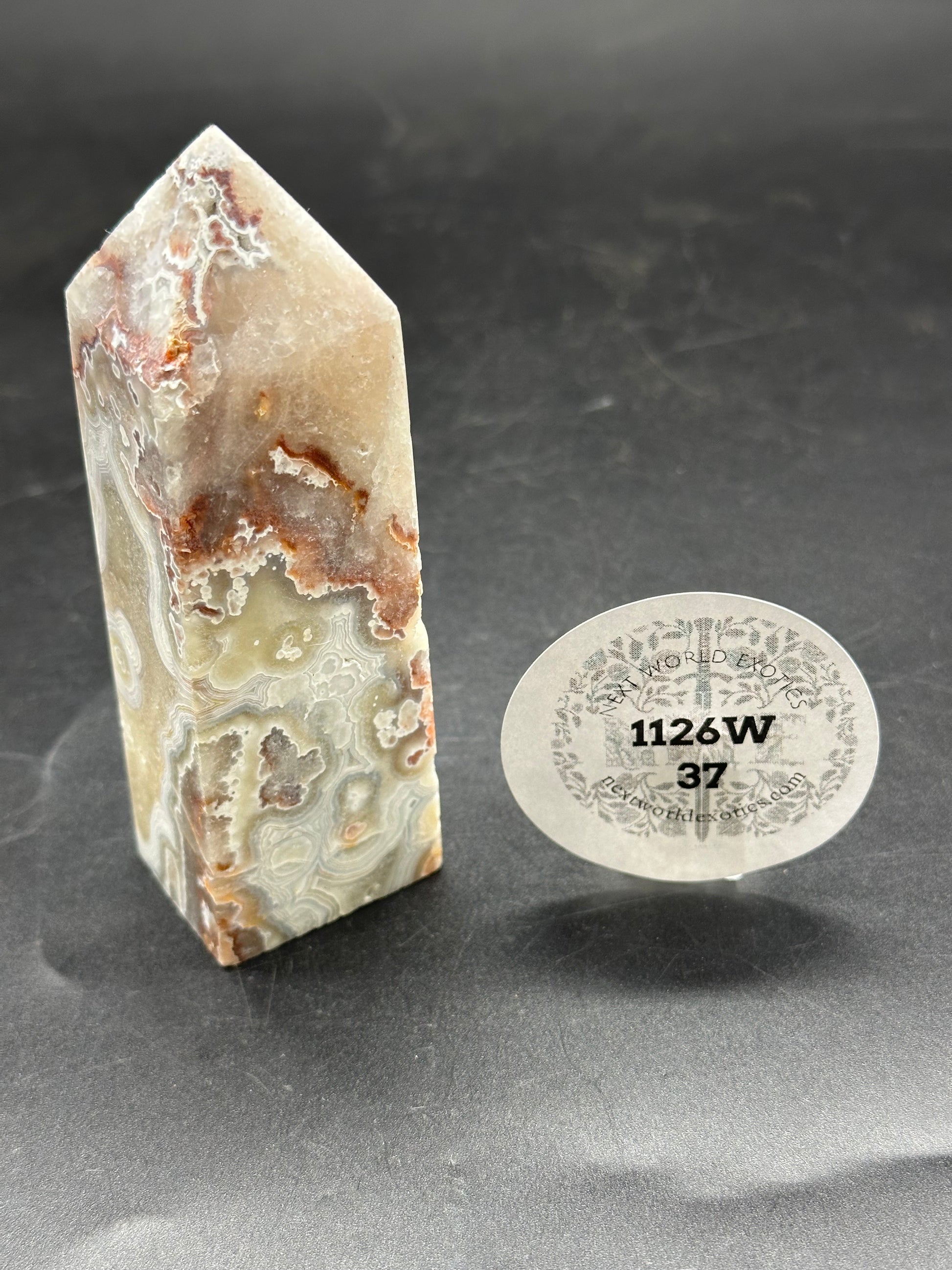 Crazy Lace Agate Tower (1126W37) displayed on a table, featuring intricate patterns, with a visible white circle containing black text and numbers nearby.
