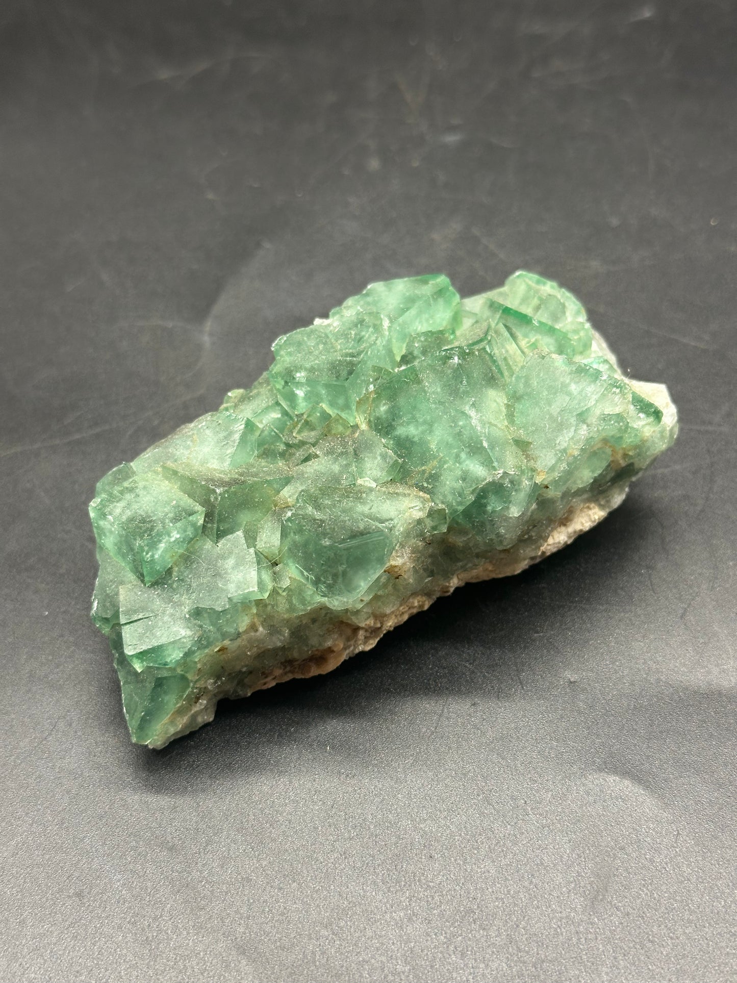 Raw Heliofluorite Carving (1212W28) showcasing a detailed green crystal structure, expertly carved from a mineral rock, displayed on a dark surface.