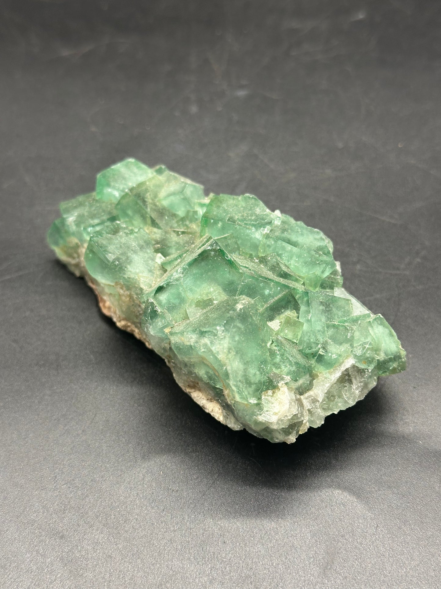Raw Heliofluorite Carving (1212W28) displayed on a black surface, highlighting its intricate green crystal structure and natural mineral formation.