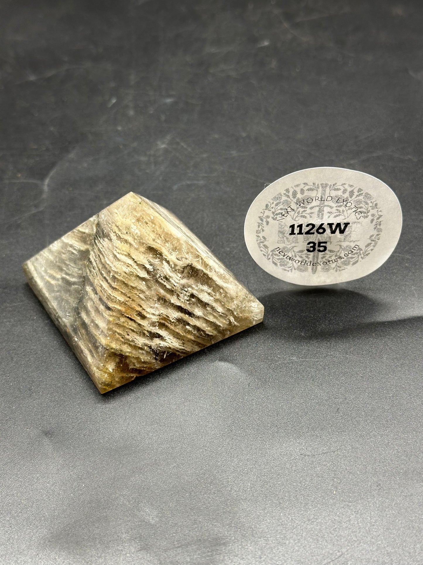 Thousand Layer Quartz Pyramid (1126W35) next to a circular label with numbers. Close-up highlights the pyramid's intricate layers and precise geometric form.