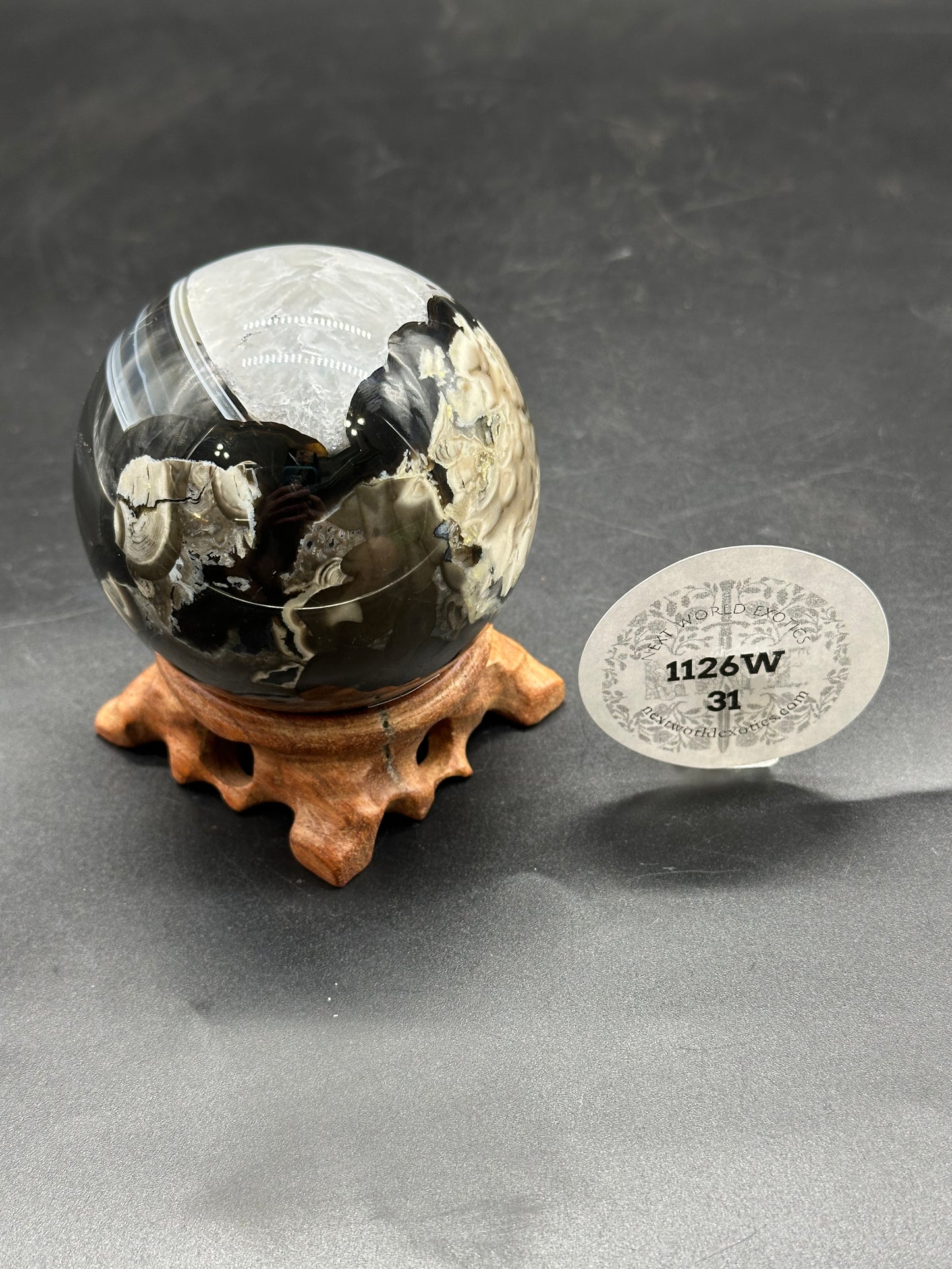 Volcanic Agate Sphere (1126W31) on wooden stand with circular label, featuring reflective surface and artistic, still-life presentation.
