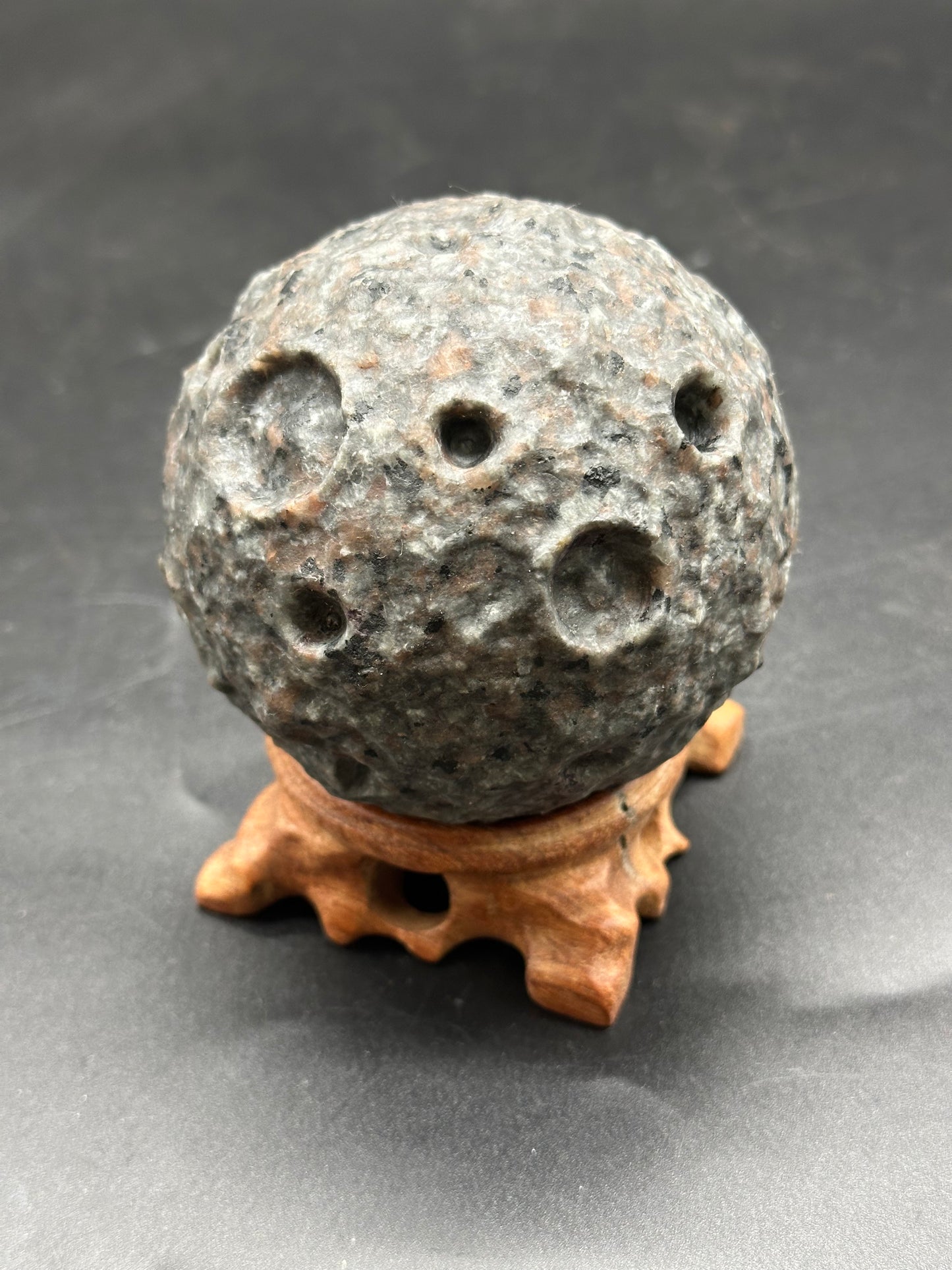 Yooperlite Moon Carving (1126W32) featuring a round stone with natural holes, elegantly displayed on a stand, highlighting its unique, textured surface.