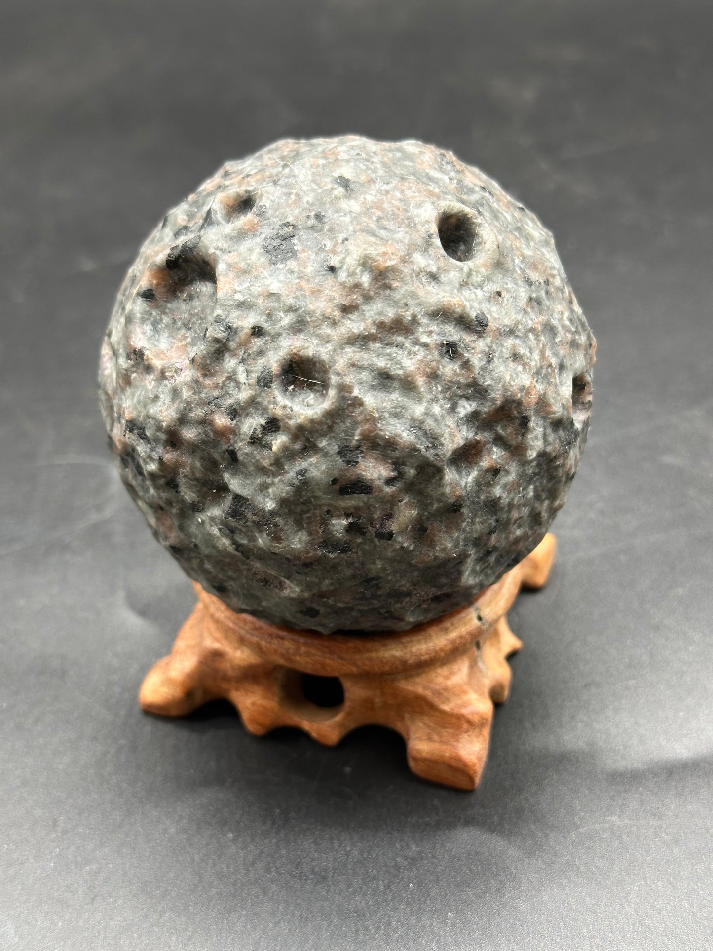 Yooperlite Moon Carving (1126W32) displayed as a smooth, round stone on a stand, highlighting its unique texture and polished surface.