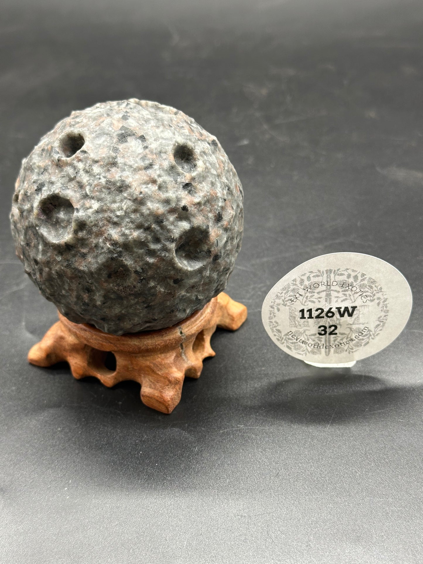 Yooperlite Moon Carving (1126W32) displayed on a wooden stand, accompanied by a round paper tag.