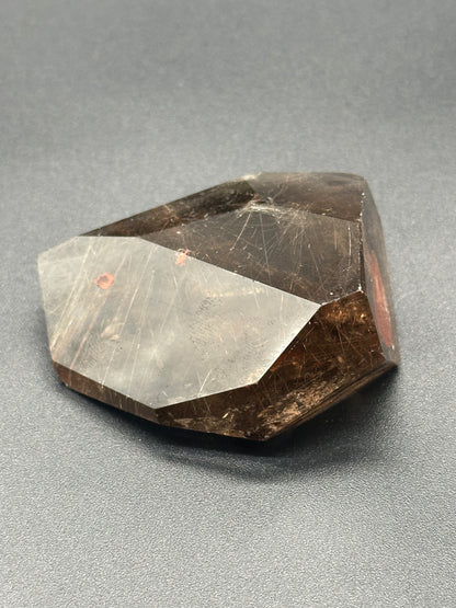 Rutilated Smokey Garden Quartz (213W05) crystal displayed on a surface, showcasing intricate mineral patterns and textures.