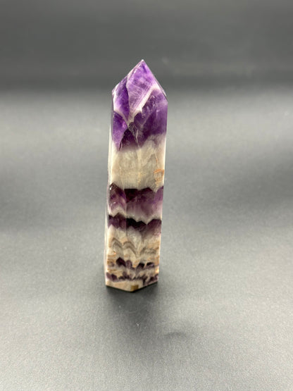 Dream Amethyst Tower (213W10): A close-up view of a polished, multi-faceted crystal with a smooth surface, showcasing its intricate structure and natural beauty.