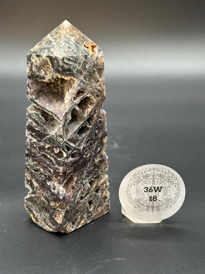 Sphalerite Tower (36W18) showcasing a rock with crystal formations and holes, accompanied by a white round sticker with black text and numbers.