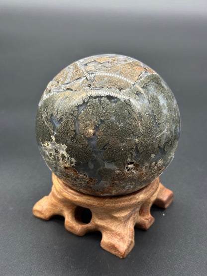 Nipomo Marcasite Sphere (36W19) featuring intricate gold patterns on a round stone, displayed on a wooden sculpture.