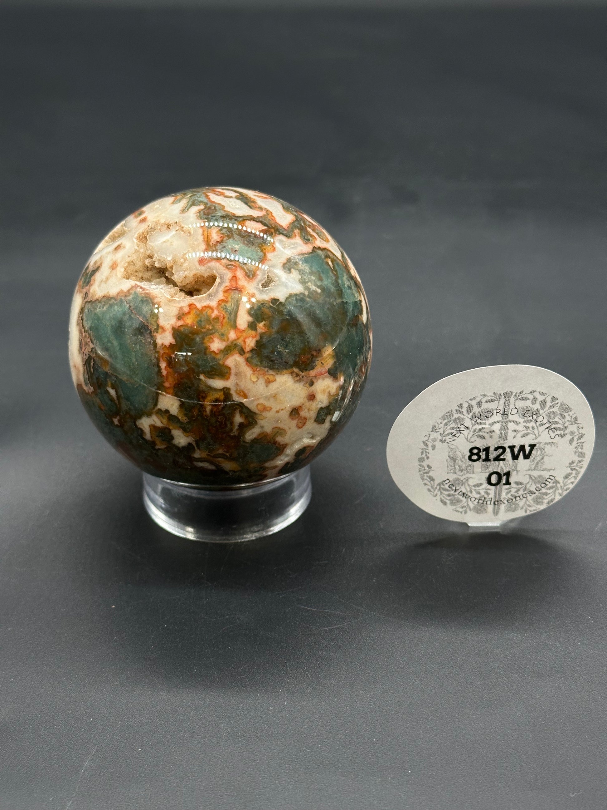 Red Moss Agate Sphere (812W01) on acrylic stand, showcasing cream, green, and rust banding with a druzy-lined cavity, accompanied by dealer's item tag.