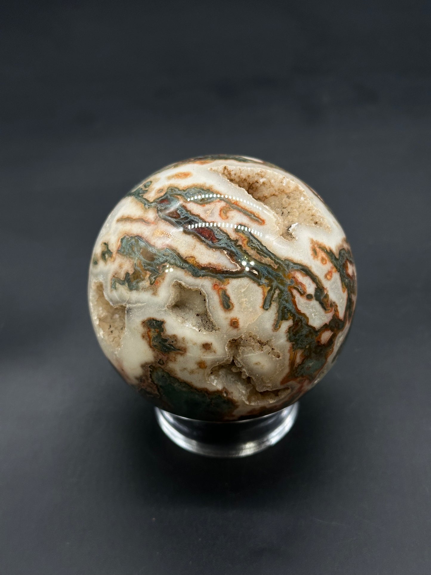 Red Moss Agate Sphere (812W01) on a clear stand, showcasing swirling bands and drusy quartz cavities, emphasizing its natural mineral beauty and craftsmanship.