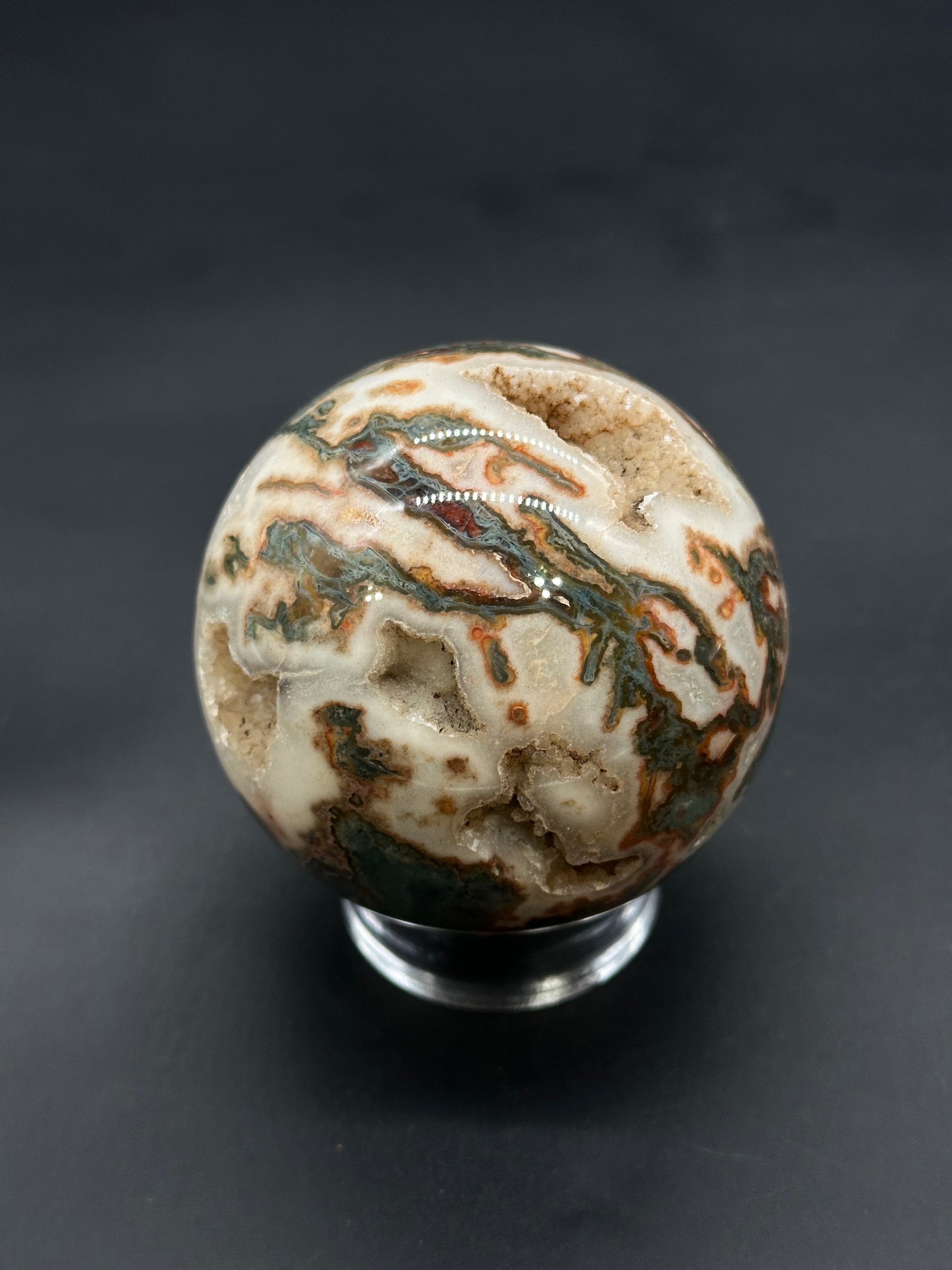 Red Moss Agate Sphere (812W01) on a clear stand, showcasing swirling bands and drusy quartz cavities, emphasizing its natural mineral beauty and craftsmanship.
