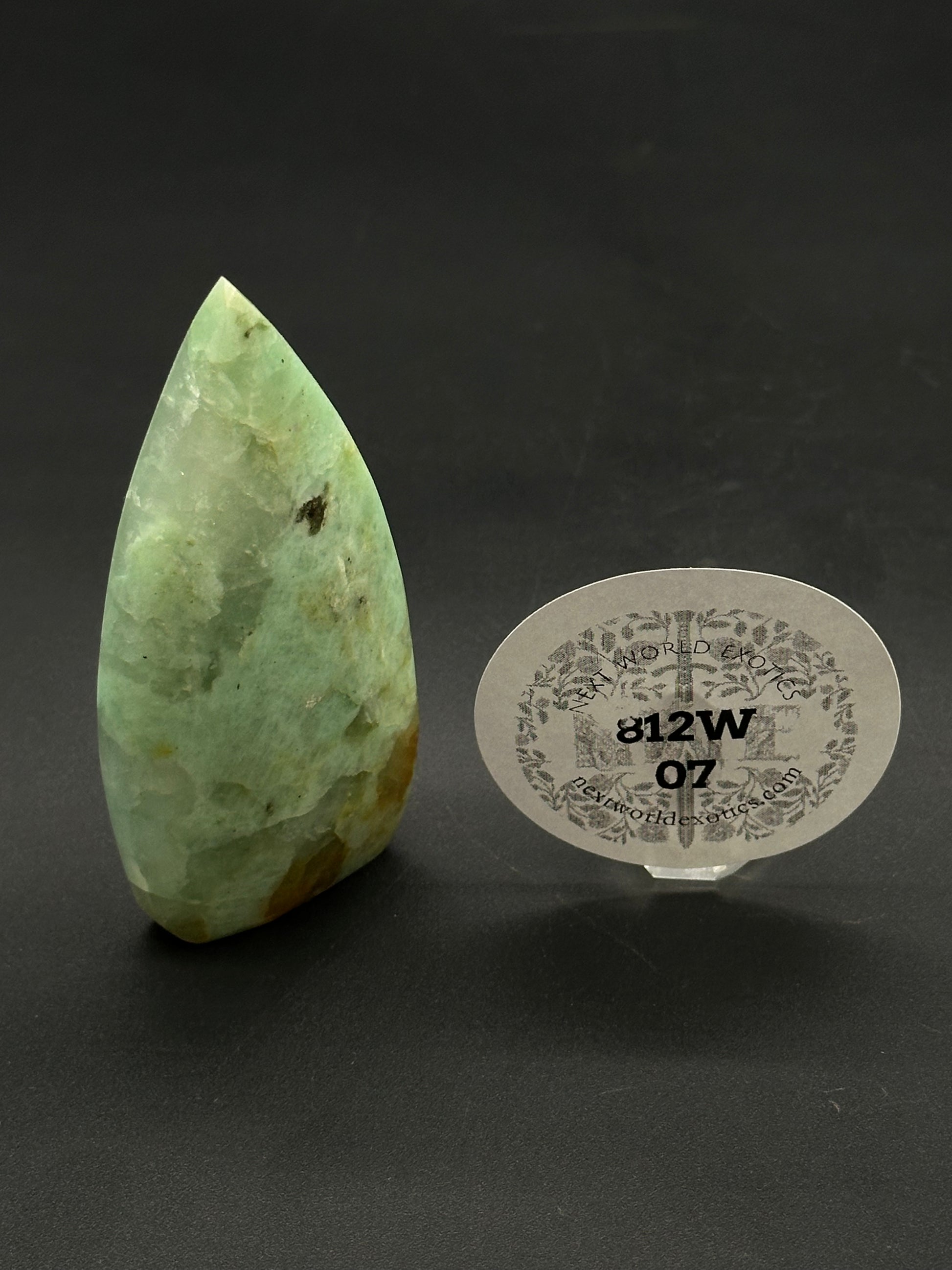 Quantum Quatro Free Form (812W07) polished green mineral specimen, featuring brown inclusions, displayed upright with a nexworldexotics.com tag from Next World Exotics.