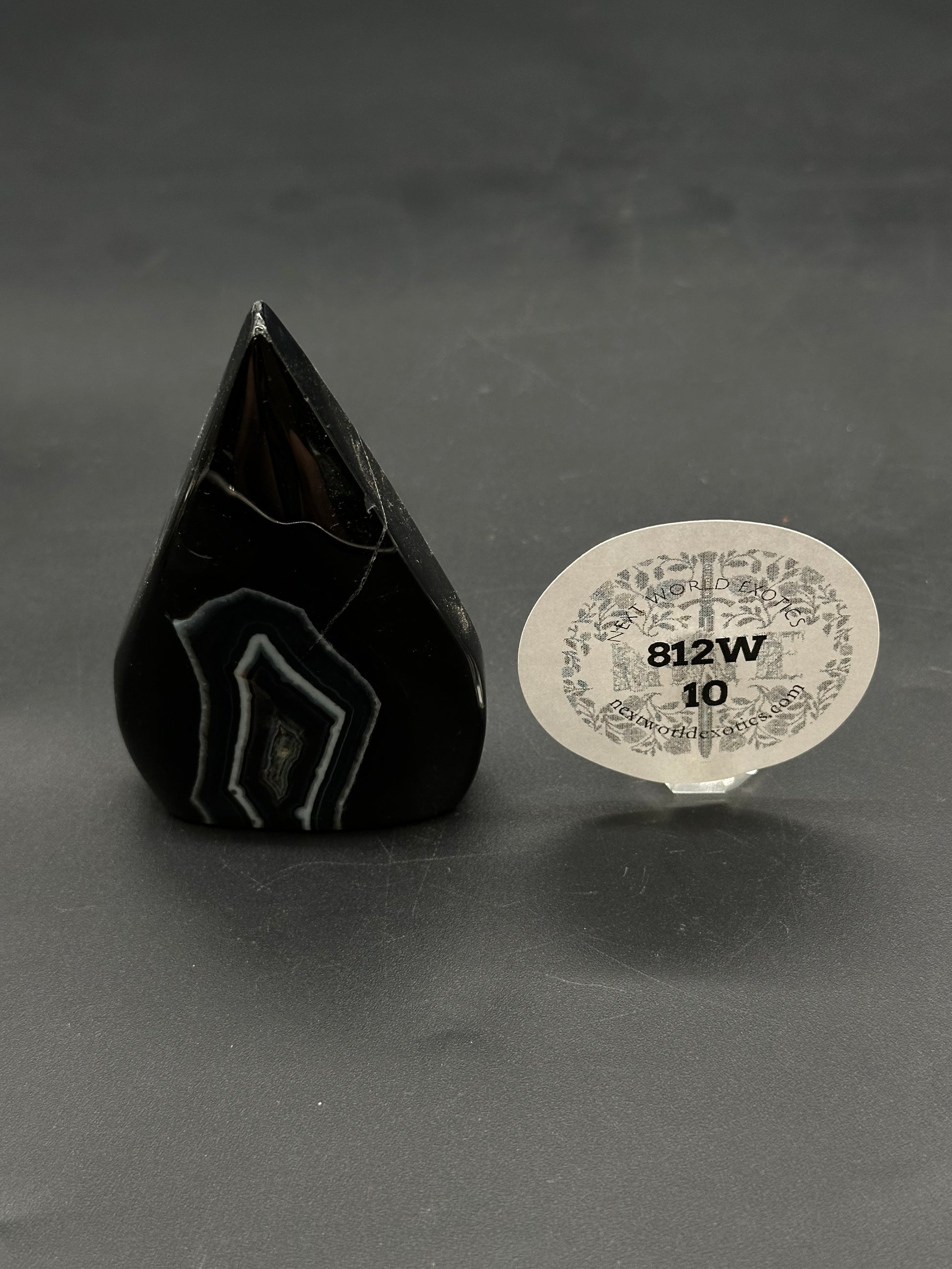 Black Agate Free Form (812W10) carved into a rounded-teardrop shape, set upright, with a small round tag reading “812W 10” nearby.