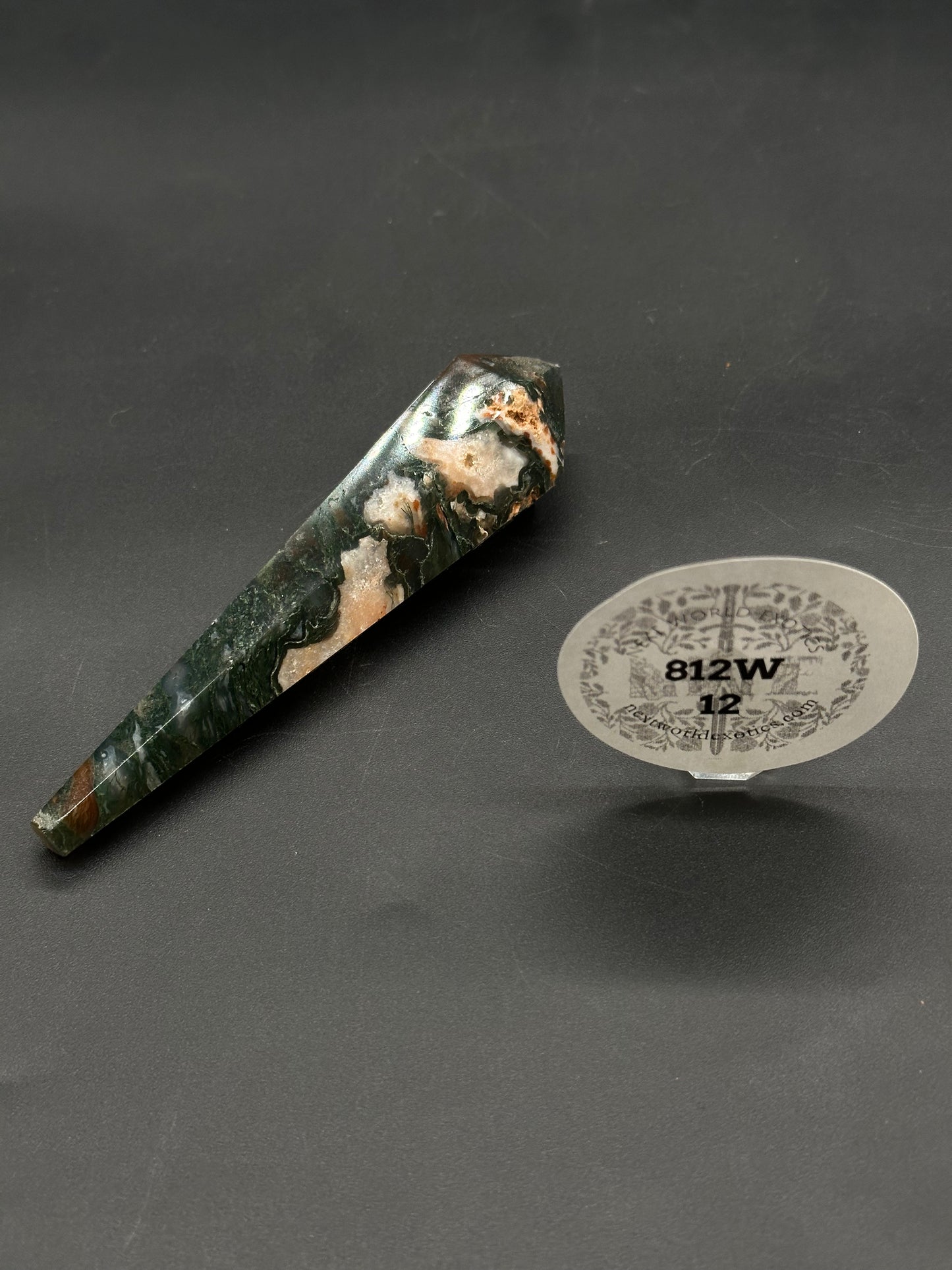 Red Moss Agate Scepter (812W12) shown as a polished hexagonal crystal wand with dark green and creamy white patterns, resting on a black mat.