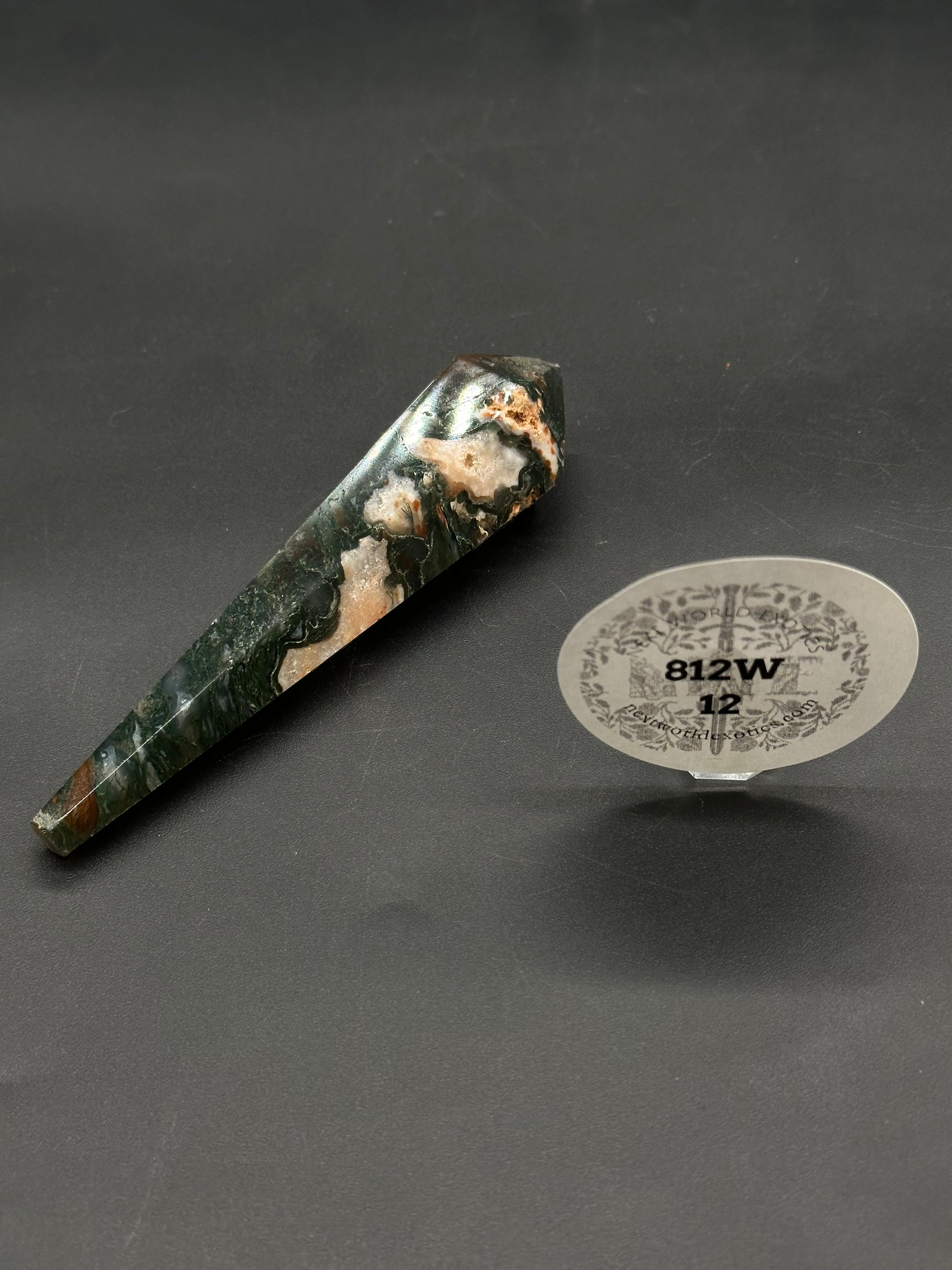 Red Moss Agate Scepter (812W12) shown as a polished hexagonal crystal wand with dark green and creamy white patterns, resting on a black mat.