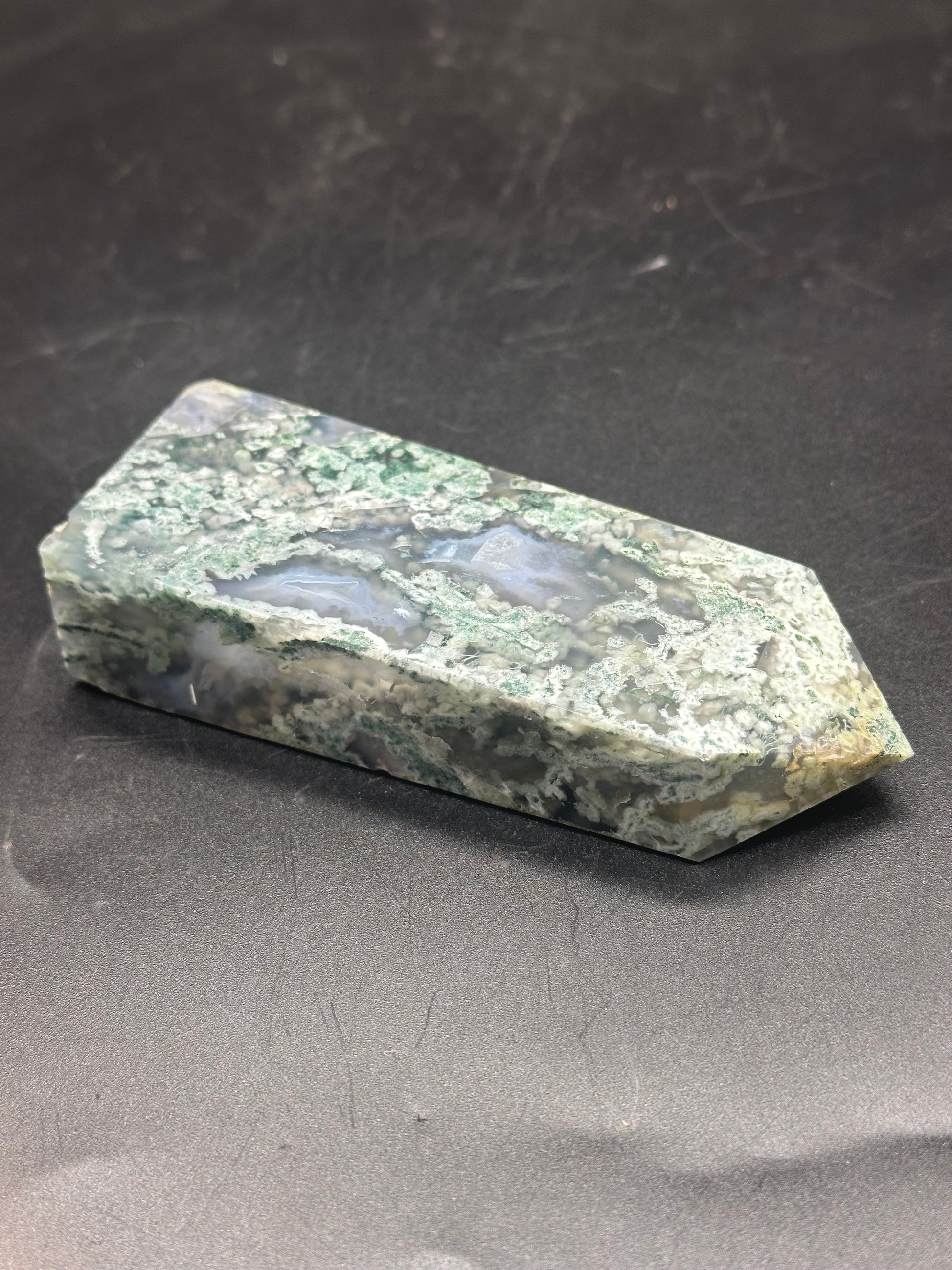 Blue Moss Agate Tower (103W49) displayed on a black surface, showcasing its intricate green and white stone patterns.