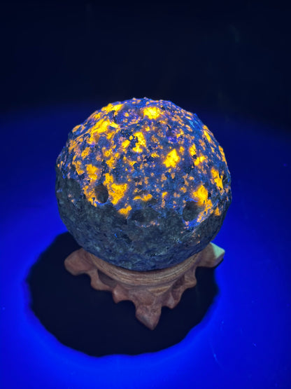 Yooperlite Moon Carving (1024W53) displayed on a stand, featuring a glowing surface with intricate patterns, highlighting its unique mineral properties.