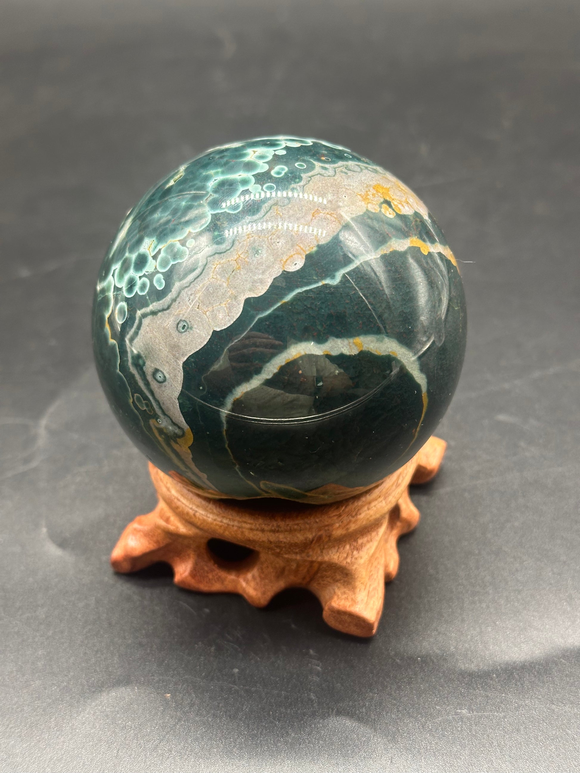 Ocean Jasper Sphere (1121W08) displayed on a wooden stand, showcasing its smooth surface and intricate patterns, ideal for crystal enthusiasts and collectors.