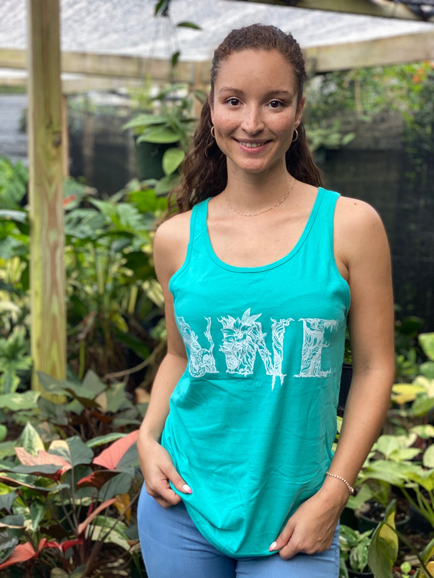 Woman in Lagoon Blue NWE Logo Tank Top smiles at the camera, showcasing the botanical floral monogram logo designed by Ashley Simone.