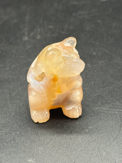 Agate Bear Carving (103W44): a small, intricately carved bear made from agate stone, displayed on a gray surface.