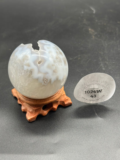 Agate Sphere with Duzy Caverns (1024W43) on a wooden stand, showcasing a prominent hole, resembling a natural mineral formation.