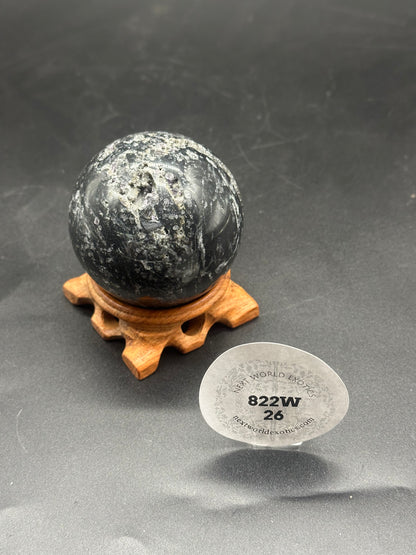 Black Sphalerite Sphere (822W26) displayed on a wooden stand, showcasing its marbled texture and natural beauty.