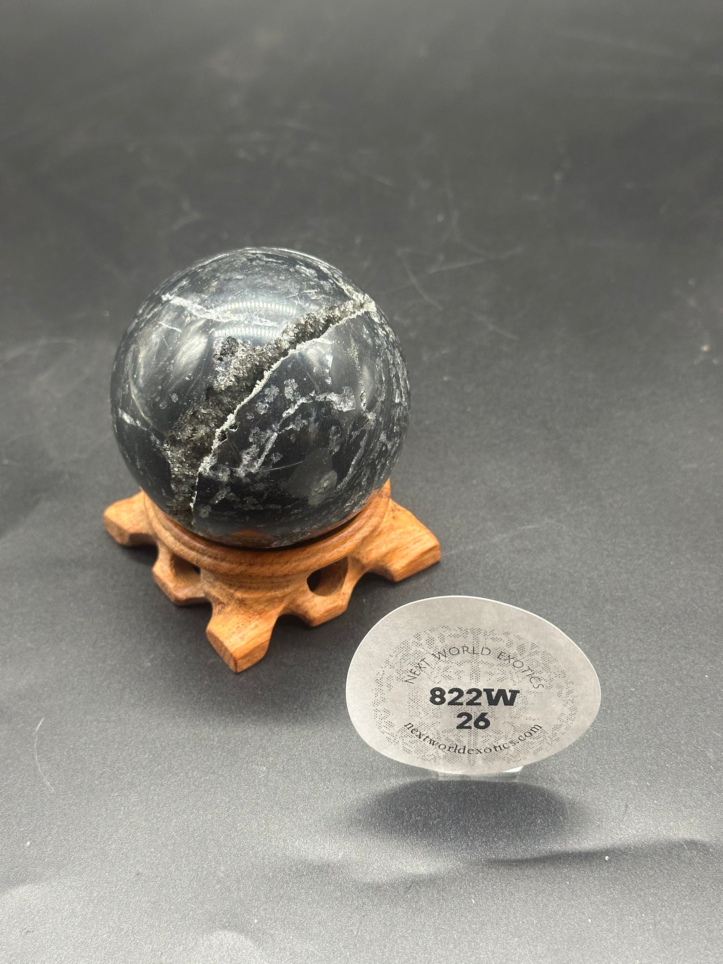 Black Sphalerite Sphere (822W26) displayed on a wooden stand. The round, stone sphere is a natural mineral, perfect for home decor or personal collections.