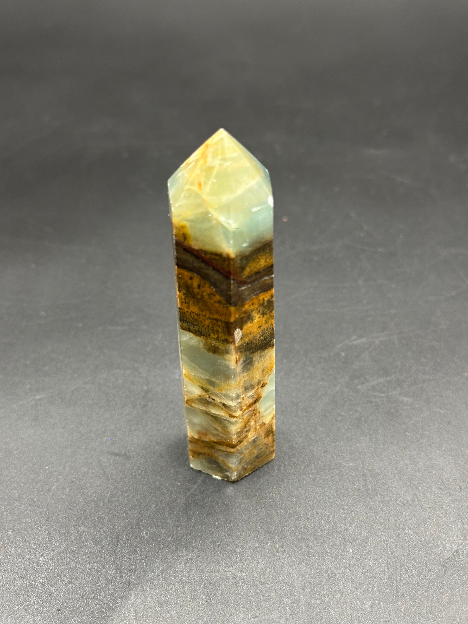 Blue Onyx Tower (123W20) displayed on a grey surface, showcasing a close-up view of its crystalline structure and mineral composition.