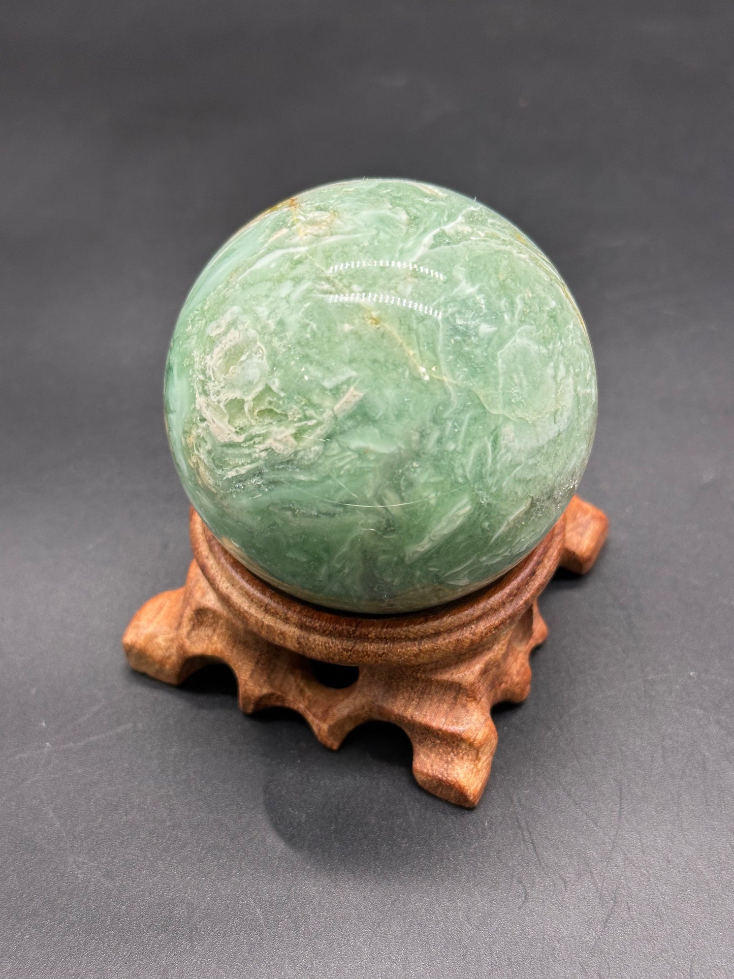 Brecciated Fluorite Sphere (123W17) displayed on a wooden stand, highlighting its polished surface and spherical shape.