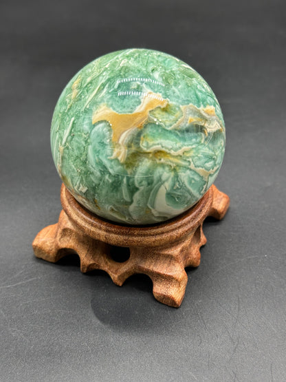 Brecciated Fluorite Sphere (123W17) displayed on a wooden stand, showcasing its polished surface and intricate patterns.