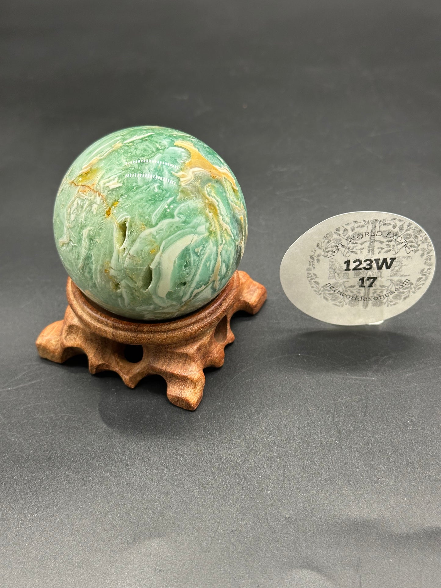 Brecciated Fluorite Sphere (123W17) displayed on a wooden stand, accompanied by a paper tag. The sphere exhibits a marbled pattern, highlighting its unique mineral composition.