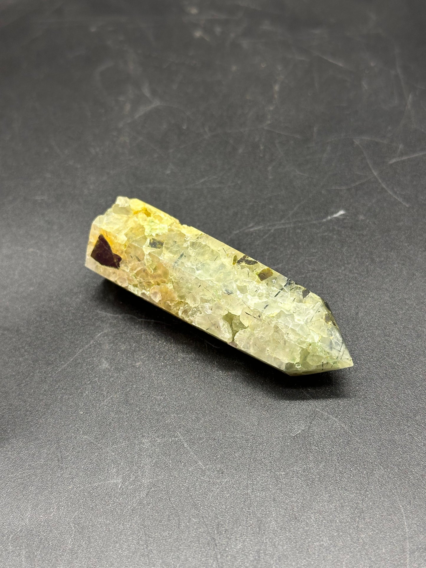 Epidote and Prehnite Tower (1017W46) displayed on a black surface, showcasing its crystalline structure and intricate details in a close-up view.