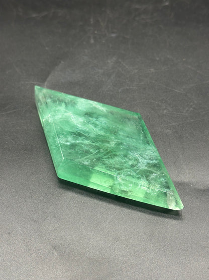 Faceted Fluorite Diamond (1212W29) with a rectangular shape and visible surface scratches, placed on a dark background.