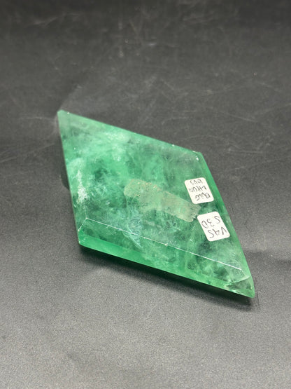 Faceted Fluorite Diamond (1212W29) on display, featuring intricate facets and a white label, set against a dark surface.