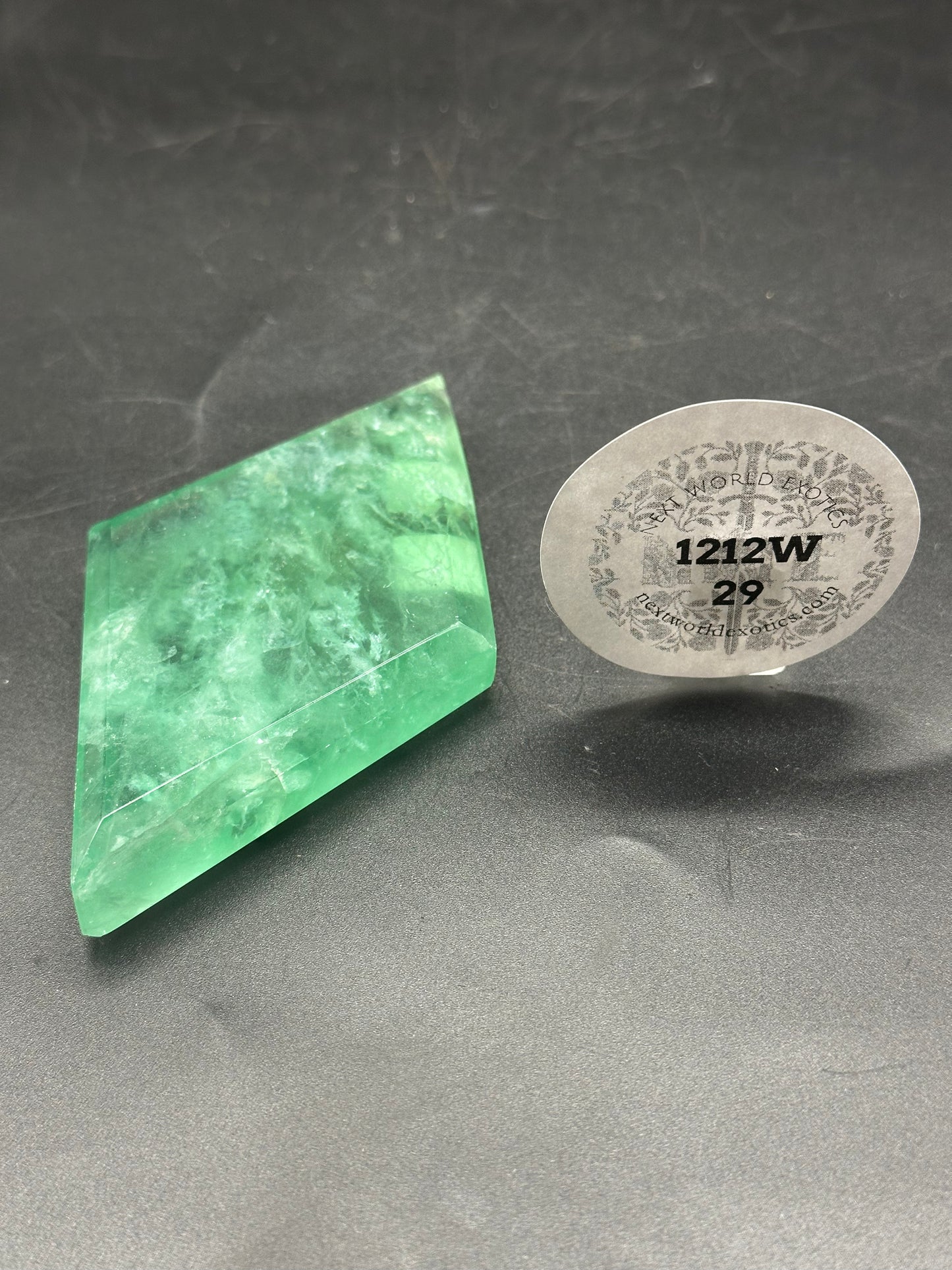 Faceted Fluorite Diamond (1212W29) displayed on a black surface, accompanied by a sticker with numbers and text, highlighting its unique crystal structure.