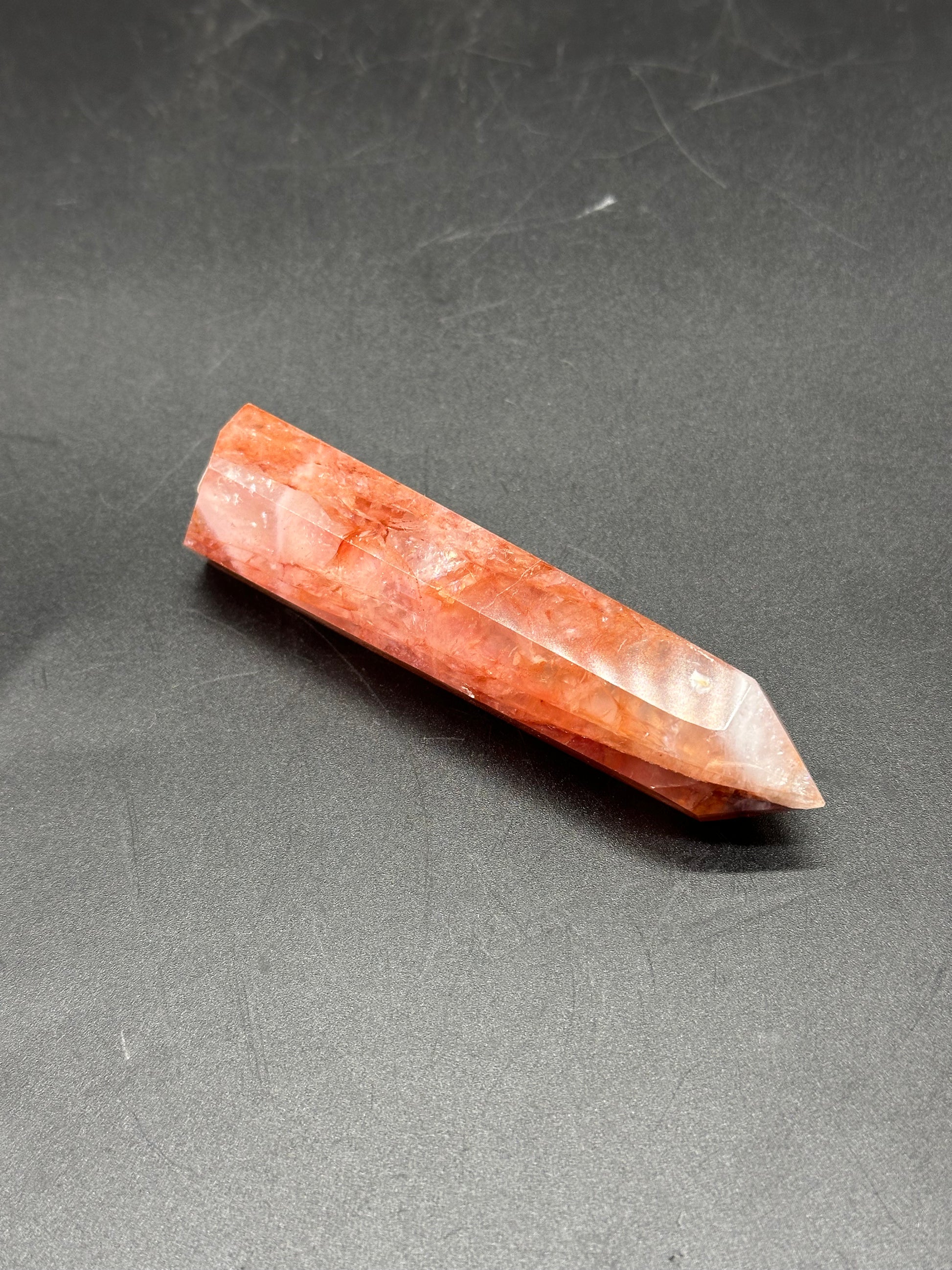 Fire Quartz Tower (1017W44) shown as a polished crystal point resting on a dark surface, highlighting its natural structure and details.