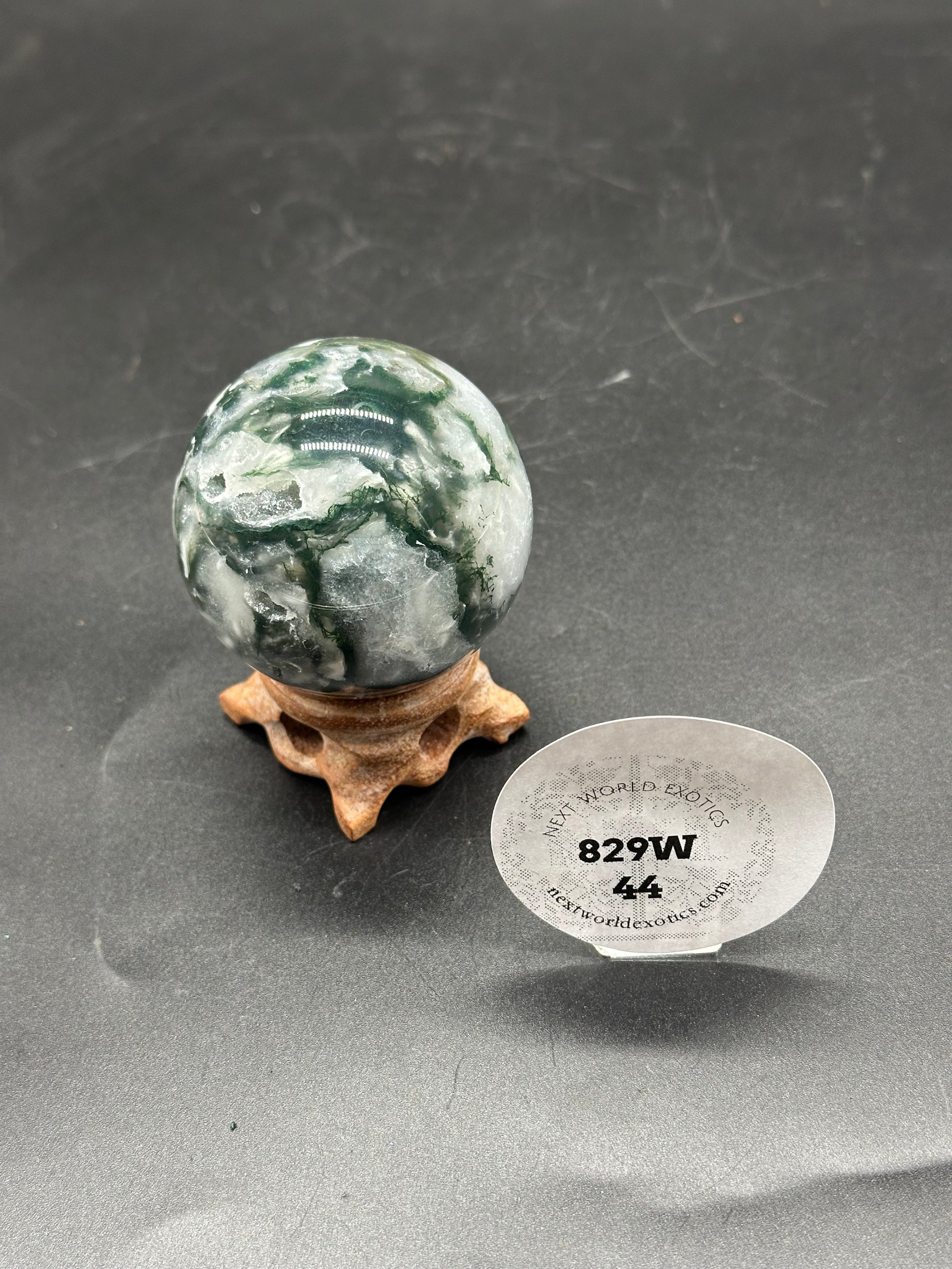 Moss Agate Sphere (829W44) displayed on a wooden stand, featuring a marbled design with a circular label.