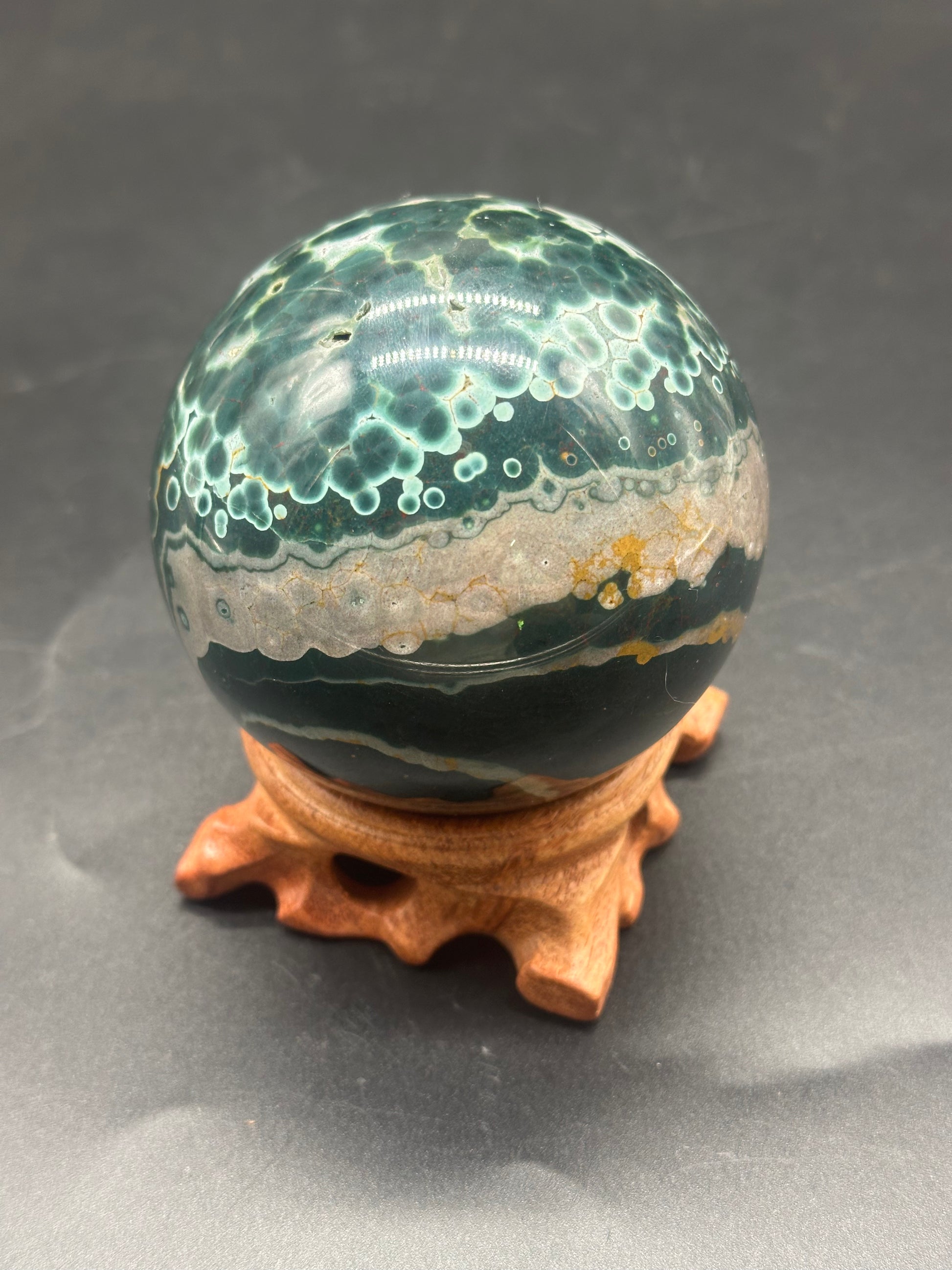 Ocean Jasper Sphere (1121W08) displayed on a wooden stand, showcasing its marbled design, highlighting its distinctive mineral composition and polished surface.