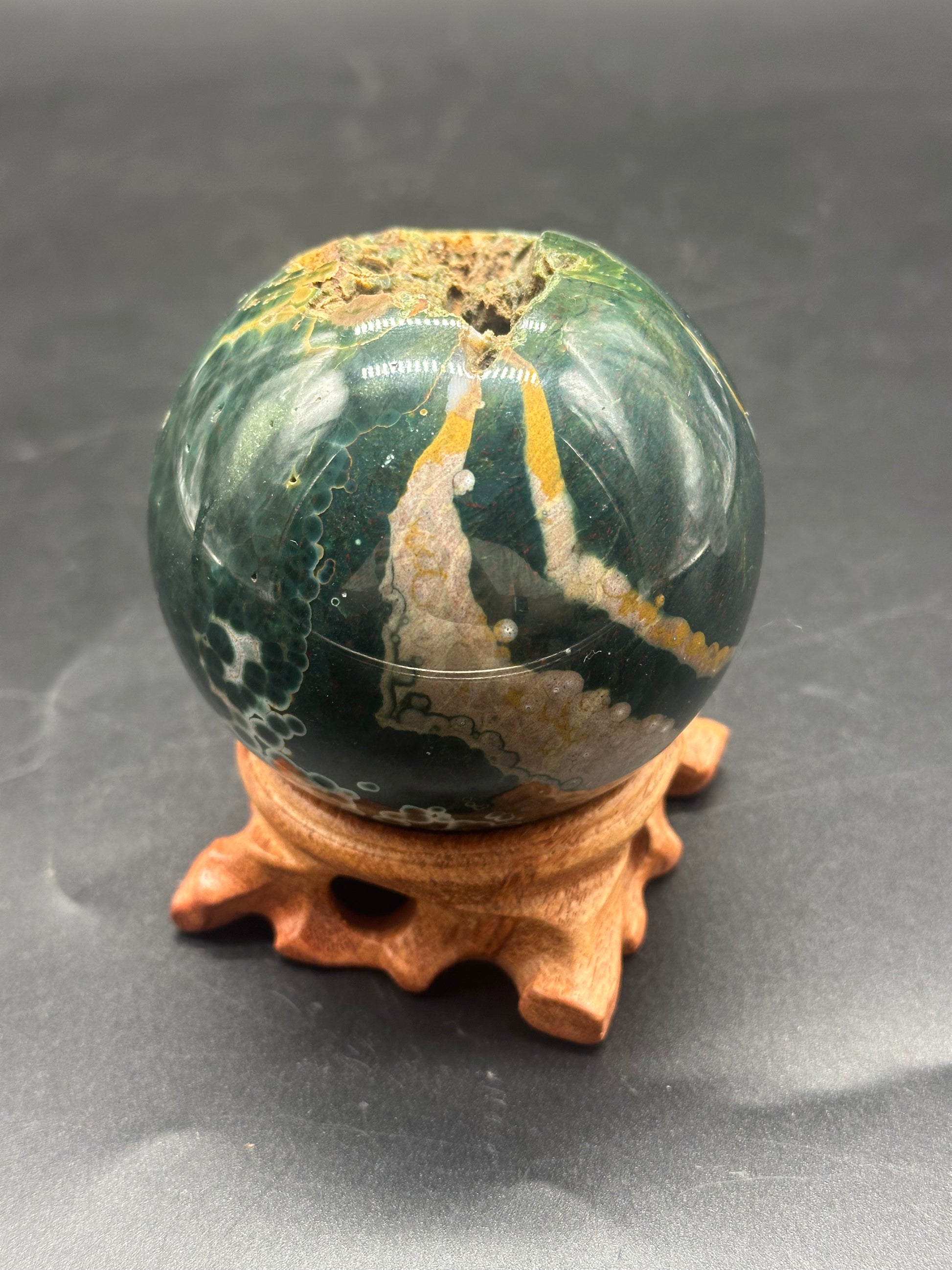 Ocean Jasper Sphere (1121W08) displayed on a wooden stand, showcasing its smooth, polished surface and intricate patterns.